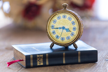 Old alarm clock on Holy bible with flowers on wooden table