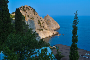 Fototapeta na wymiar top view of stone rock cliff on shore of Black Sea bay, blue water, summer, green forest, trees in the foreground, sunlight