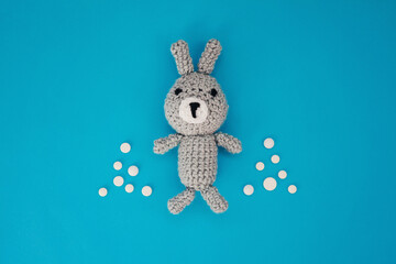 Soft toy knitted rabbit with pill christmas trees on blue background. Concept of children's health, medical care, diseases of ears, feet, treatment during holidays. Top view. Copy space.