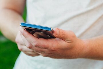 close-up shot of male hands holding smartphone with blank screen copy space for your text message or information content, against green nature background