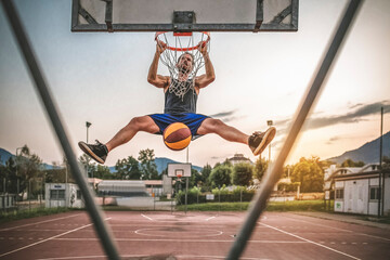 Young man does a slam dunk playing outdoor basketball.