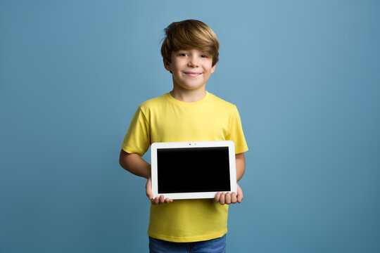 Portrait of happy little child show the digital tablet on blue background.