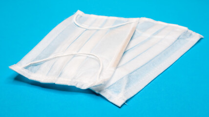 Two three-layer disposable surgical face masks with rubber pads to cover the mouth and nose against a blue background. The concept of protection from bacteria, healthcare and medicine. COVID-19.