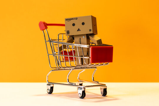 Small Amazon figurine with a supermarket cart on a orange background - online store and commerce - promotion, black friday