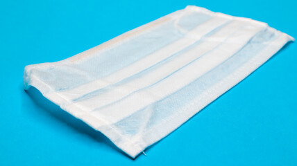 One 3-ply disposable surgical face mask with rubber grips covering mouth and nose against blue background. Protection from bacteria, healthcare and medicine concept. COVID-19. A dangerous virus.