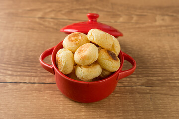 Traditional Brazilian Snack Cheese Bread in a rustic red cooking pot. On a wooden table background. with copy space