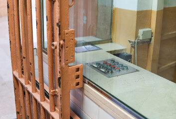 Remote сontrol desk with a bunch of buttons in the security room of an old-fashioned prison or jail with cell door made of steel metal bars painted with orange peeling paint.