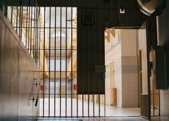 View on the prison corridor through the jail cell door made of steel metal bars with the old lock and peeling paint.