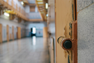A closeup of the lock of a brick jail cell with the latch. Old-fashion worn-out prison latch with beige peeling paint on the jail cell door.
