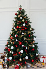 Christmas tree with gifts of garland lights for the new year in the interior of the white room as a backdrop