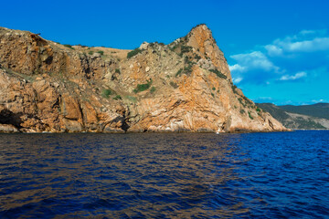 Fototapeta na wymiar red stone rock stands on shore of the blue sea on a bright sunny day, summer sky with clouds