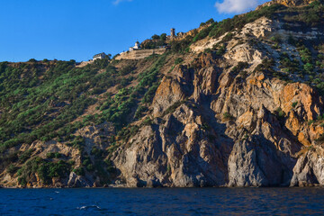 Fototapeta premium red orange stone cliff with green grass and tress stands on shore of Black sea on a bright sunset, summer sky with clouds