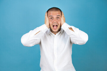 Russian business man wearing white shirt standing over blue background surprised with hand on head...