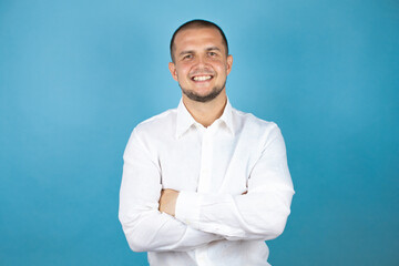 Russian business man wearing white shirt standing over blue background happy face smiling with crossed arms looking at the camera. Positive person.