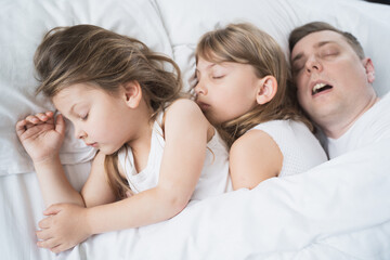 Kids, daughters, dad sleep together in bed on pillows under blanket. Father is snoring hard. Family joint sleeping. Insomnia, night bedtime.Sweet dreams. arly wake up,rise to kindergarten,school,work