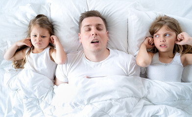 Kids, dad sleep together in bed. Father is snoring hard, girls, daughters are plugging ears with hands. Disorders, joint sleeping. Insomnia, night bedtime. Wake up, rise to kindergarten, school, work