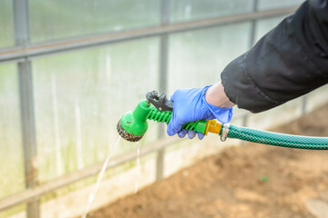 Hand in glove holds watering hose/hand in a blue glove holds a green watering hose.