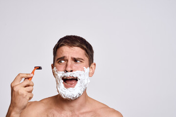 Handsome man with white shaving foam on his face and clean skin with razor grooming bare shoulders