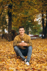 Obraz premium Portrait of handsome and happy boy smiling and drinking coffee in the autumn park