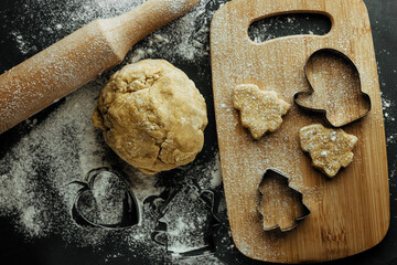 close up of christmas baking background. raw homemade rolled dough in focus and cut out shapes on kitchen board. cookie cutters and rolling pin. top view.
