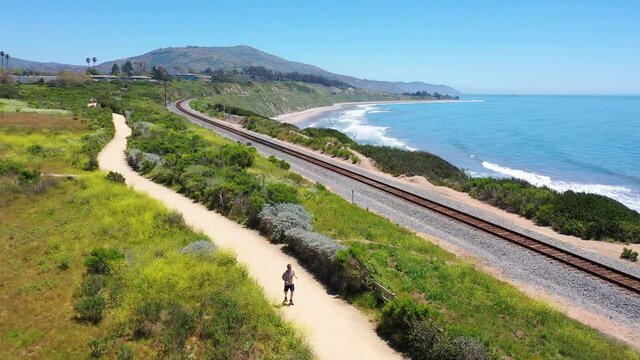 Aerial over man jogging runner exercise along coastal trail, railroad tracks and the Pacific coast near Carpinteria, Santa Barbara, California. 