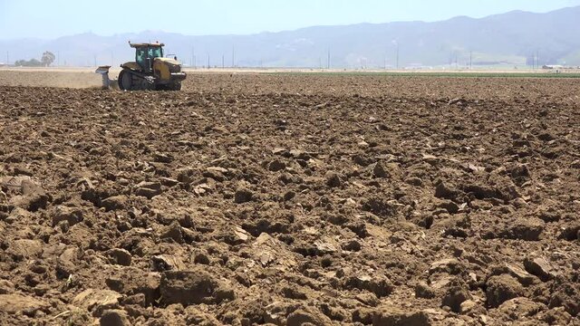 Farm tractor moves across dry dusty landscape in California suggesting drought and climate change.