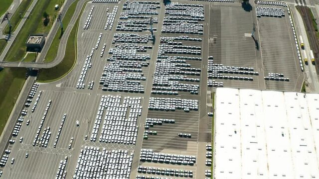 Aerial video of stock car parking. Flying over big industrial zone with big parking lot of brand new cars. Many cars waiting for sale and transportation. Automobile industry.
