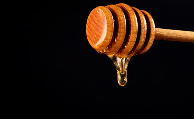 Honey dripping from wooden honey dipper on black background.