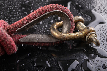 A wet shackle and a gray rope with a sailing knot. Accessories for sailors to operate boats covered with water drops. - obrazy, fototapety, plakaty