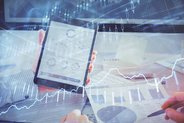 Double exposure of man's hands holding and using a digital device and forex graph drawing. Financial market concept.