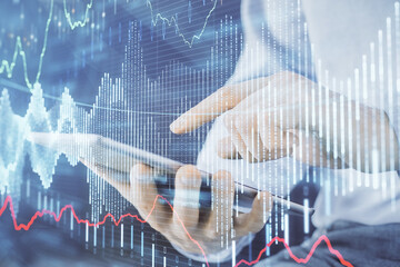 Double exposure of man's hands holding and using a digital device and forex graph drawing. Financial market concept.