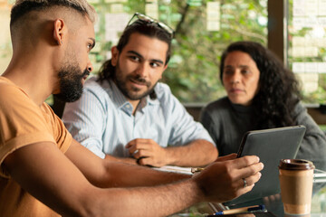 Professional latin teammates with tablet collaborating and discussing project plans in office or coworking space. Collaboration, creative, discussion, meeting concept..