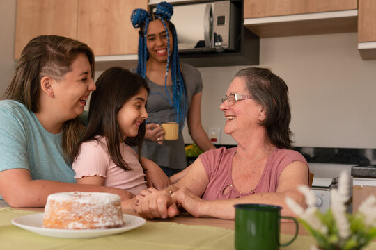 Joyful brazilian lesbian couple with daughter spending good time together with family. at kitchen table, inside. Lgbtq family, happiness, multi generation concept..