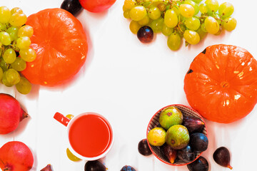 Orange pumpkins, berries of grapes and ginger, a red mug with juice on a white background, arranged along the contour, place for text,view from above.Frame of autumn fruits, vegetables and berries