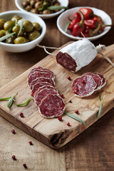 Sliced french salami with fresh rosemary and olives on rustic wooden background.	
