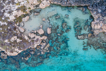 An aerial view of the beautiful Mediterranean Sea, where you can see the cracked rocky textured underwater corals and the clean turquoise water of Protaras, Cyprus,
