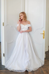 Fototapeta premium A bride in a chic wedding dress stands near the door and looks to the side