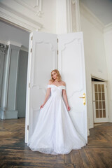 A bride in a chic wedding dress stands near the door and looks to the side