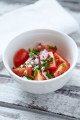 Simple salad with cherry tomatoes, red onion and fresh herbs. Bright wooden background. Close up.