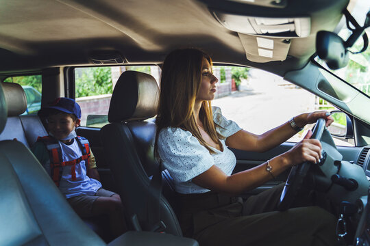 Side View On Caucasian Woman Driving Her Little Son In Car - Mother Taking Small Boy First Grade Pupil To School - Morning Daily Routine Motherhood Concept