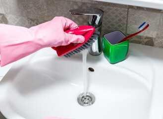 Woman hands in pink rubber gloves cleaning washing sink in bathroom. Close up. Disinfection of...