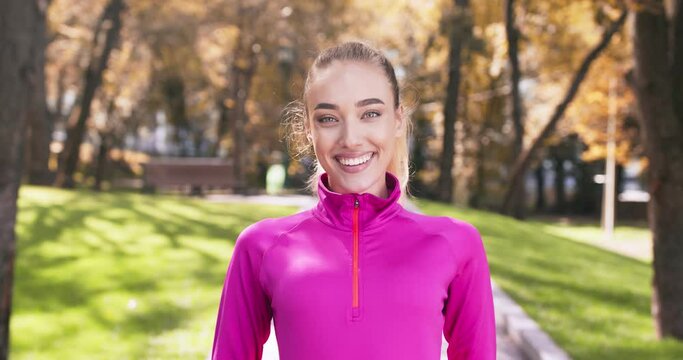 Positive blonde woman locking zipper on her pink sportswear and smiling to camera