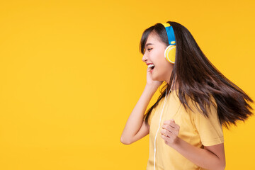 Cheerful enjoy young woman wearing headphones listening to music form smartphone and dancing relax over isolated yellow background. Lifestyle leisure with hobby concept.