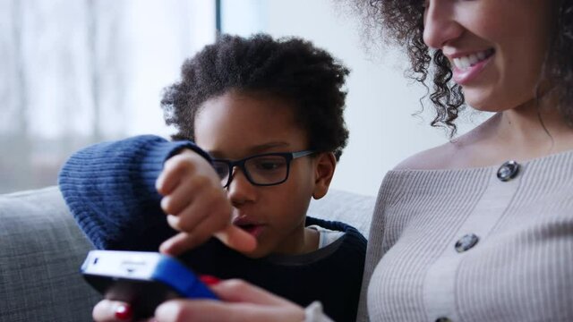 Mother and son sitting on sofa at home playing computer game together on hand held device at home - shot in slow motion