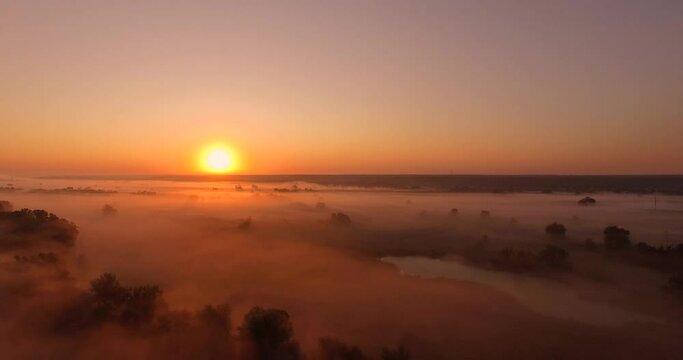 Aerial view of pink sunrise on misty valley of Siverskyi Donets river near Zmiiv city, Ukraine. Forward camera movement