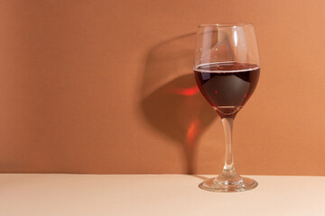 The wineglass with red wine isolated on beige background. The shadow on the wall. The drink of the gods.