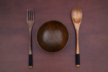 Wooden fork, spoon and bowl on wooden table, top view