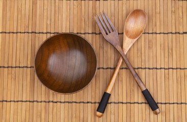 Wooden fork, spoon and bowl on bamboo place mat, top view 