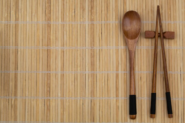 Wooden spoon and chopstick on bamboo place mat with copy space, top view 