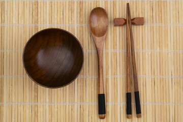 Wooden spoon, chopstick and bowl on bamboo place mat, top view 